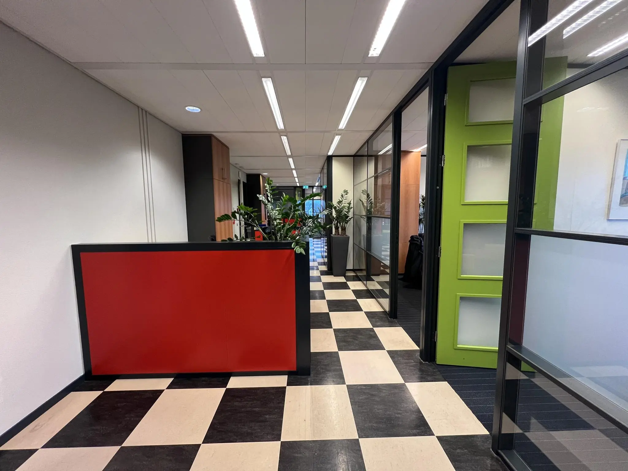 Moderne kantoorhal aan de Jacques Dutilhweg met zwart-wit geblokte vloer, rode balie en groene deur.